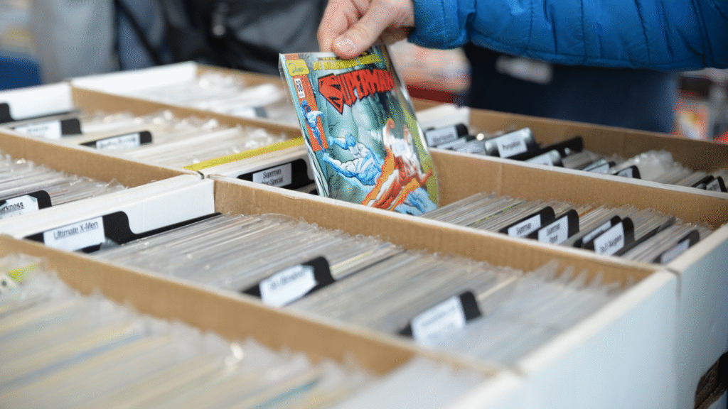 A person holding a Superman comic above a box of neatly organized comics in protective sleeves at a comic book fair.